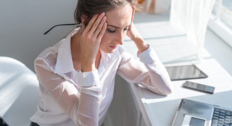 Portrait of tired young business woman suffering from headache in front of laptop at office desk.